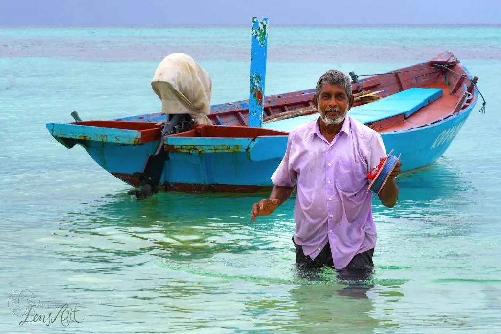 Einheimischer steht im flachen türkisen Wasser vor einem bunten Holzboot
