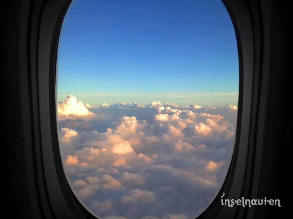 Blick durchs Flugzeugfenster auf ein Wolkenmeer in der Abenddämmerung