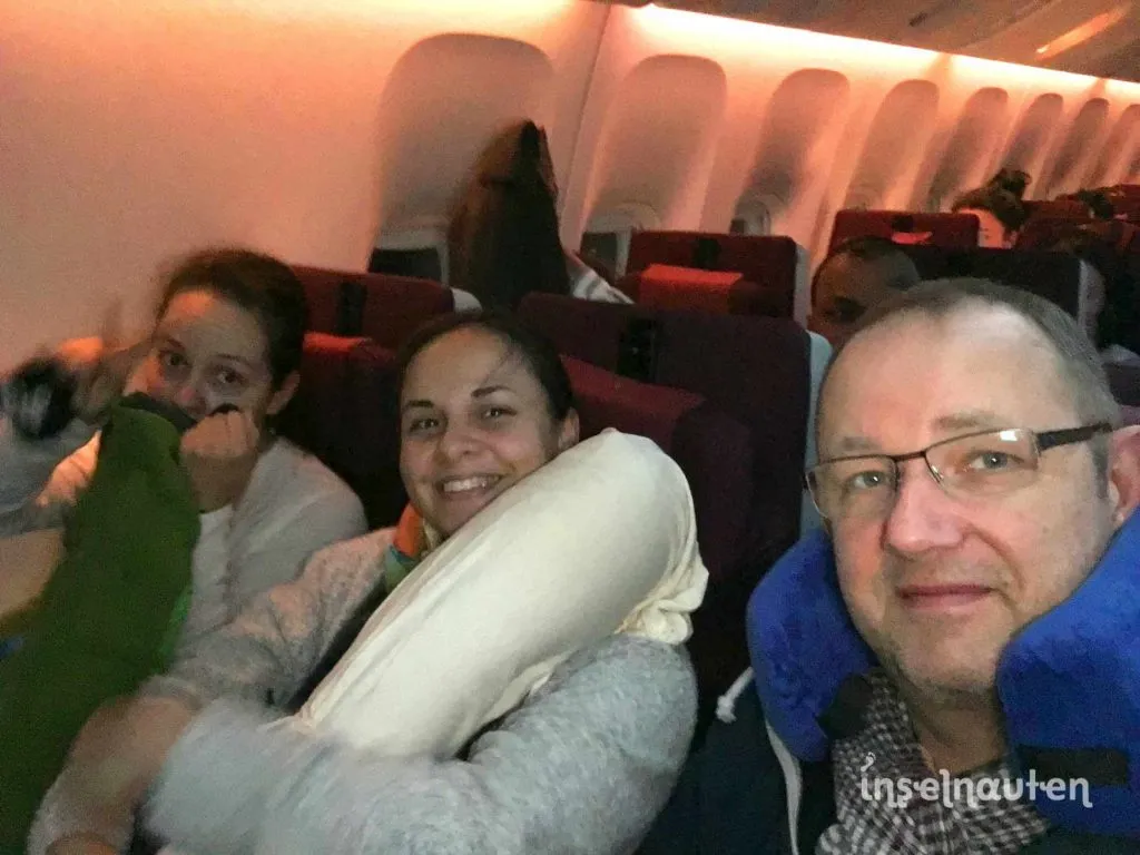 Drei Inselnauten mit Nackenkissen in der Flugzeugkabine