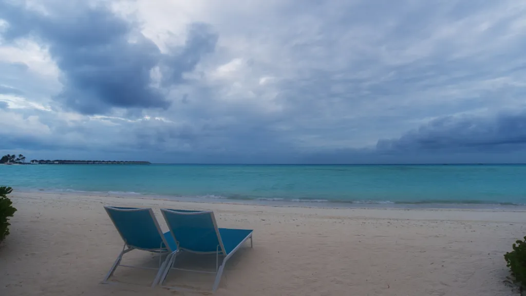 Malediven Regenzeit Panorama Zwei leere Strandliegen an einem menschenleeren Strand unter bewölktem Himmel