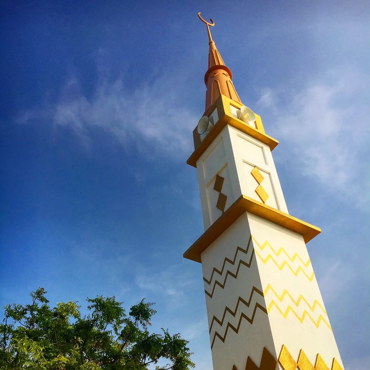 Weiß-goldenes Minarett einer Inselmoschee vor blauem Himmel
