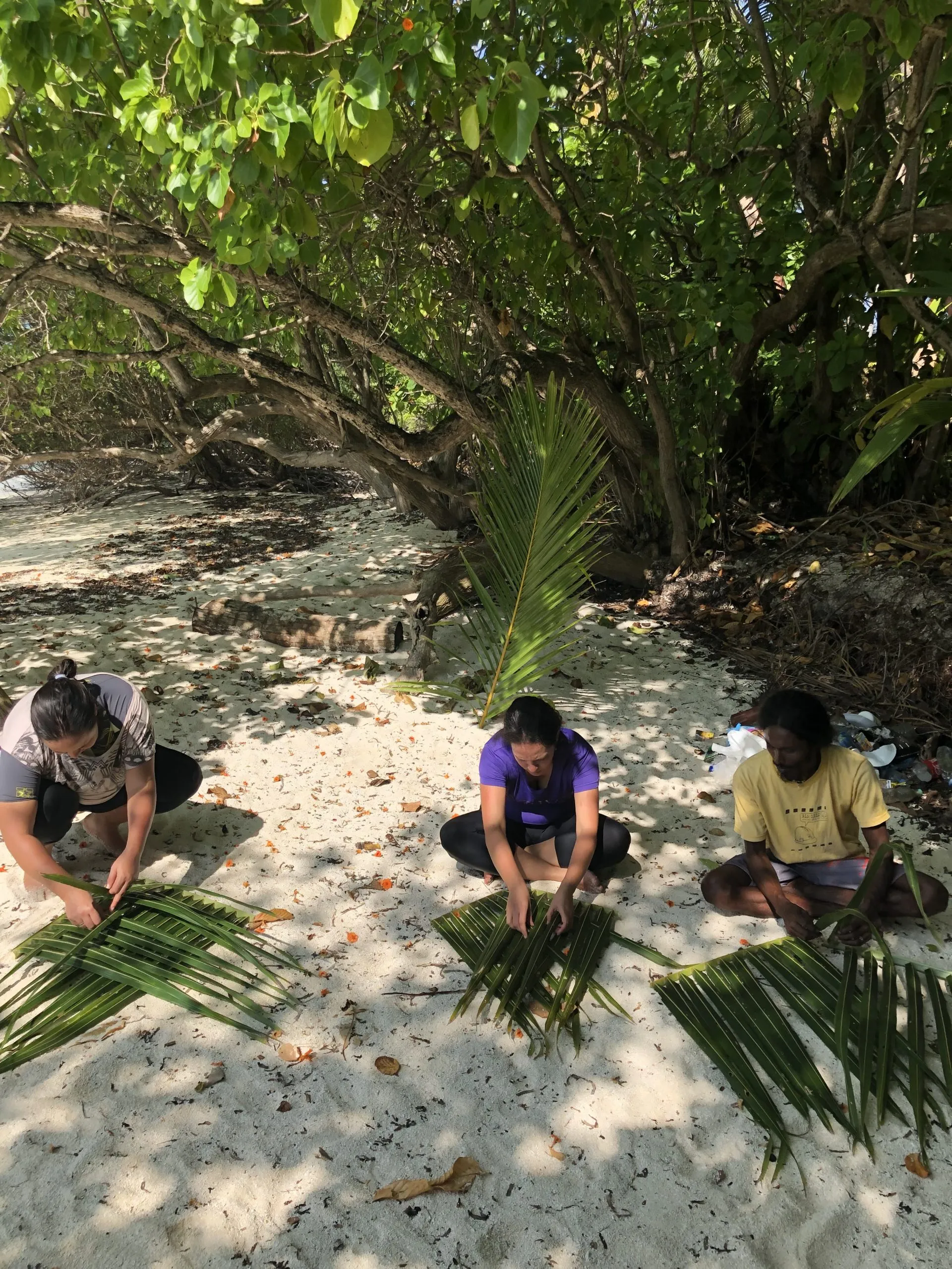 Gäste flechten mit dem Gastgeber Palmwedel am Strand