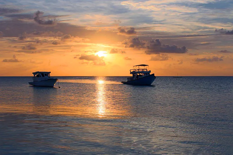 Goldener Sonnenuntergang über der Lagune mit zwei Dhoni-Booten als Silhouette