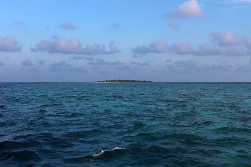Kleine grüne Malediven-Insel am Horizont zwischen endlosem blauen Meer und Himmel