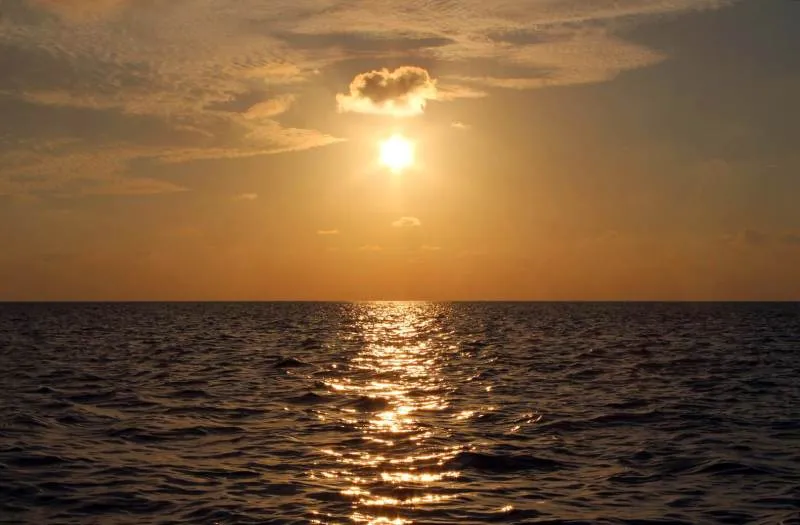 Tief stehende, goldene Sonne über dem offenen Meer mit glitzerndem Lichtpfad