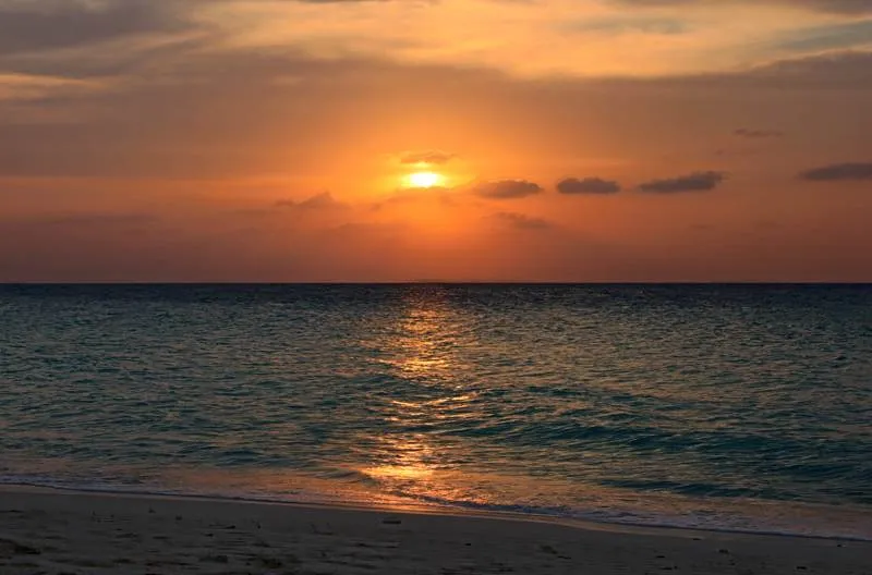 Kräftig orangefarbener Sonnenuntergang über dem Meer, vom Strand aus gesehen