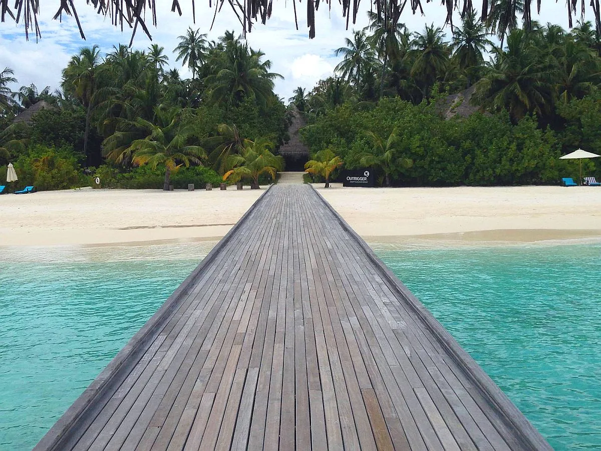Holzsteg, der über die türkise Lagune zu einer Resortinsel mit Palmen führt